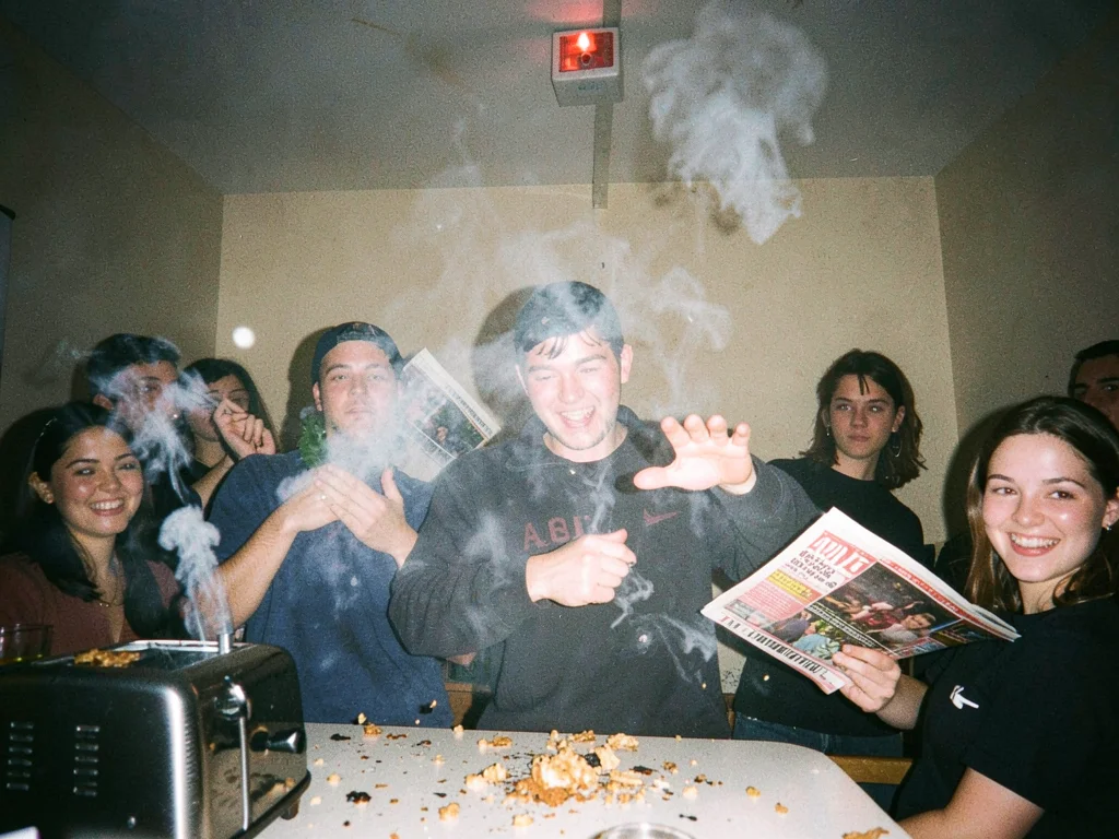 Smoke billowing from a toaster, person fanning frantically with a magazine, burn