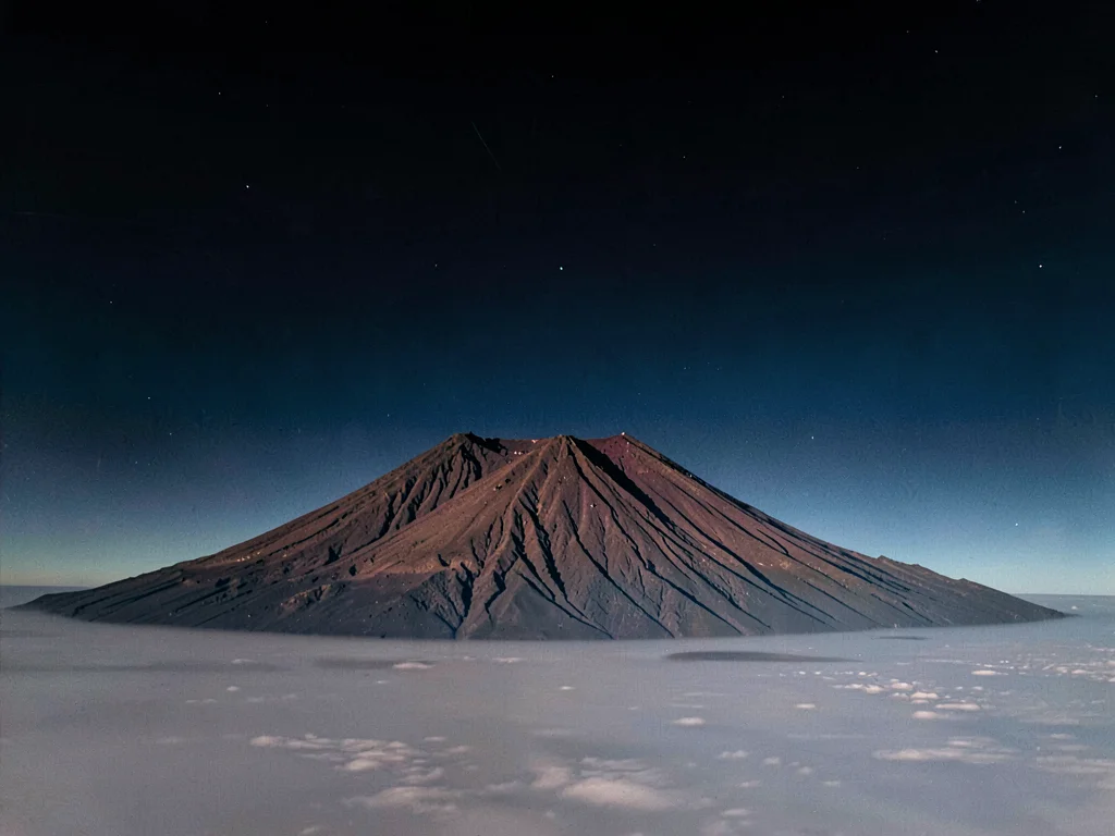 Volcanic peak rising above inversion layer into clear dark upper atmosphere