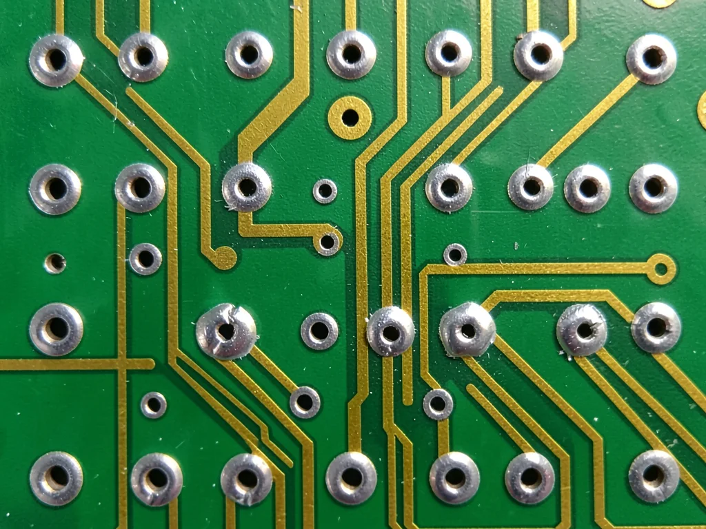 A macro of solder joints on a wave-soldered through-hole PCB — shiny silver fill