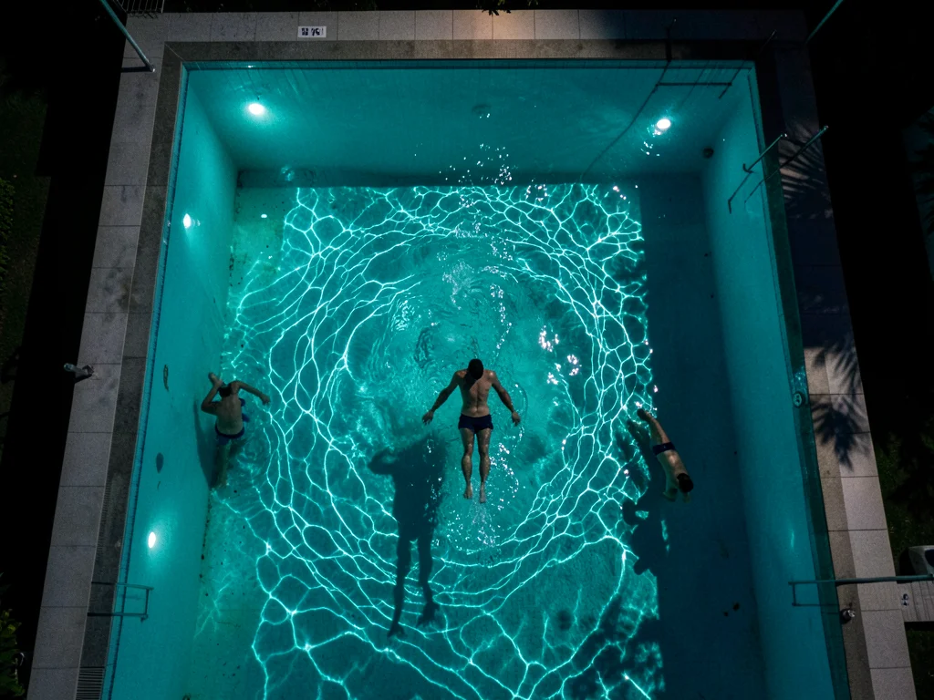 A pool at night from above, underwater lights creating a glowing turquoise recta