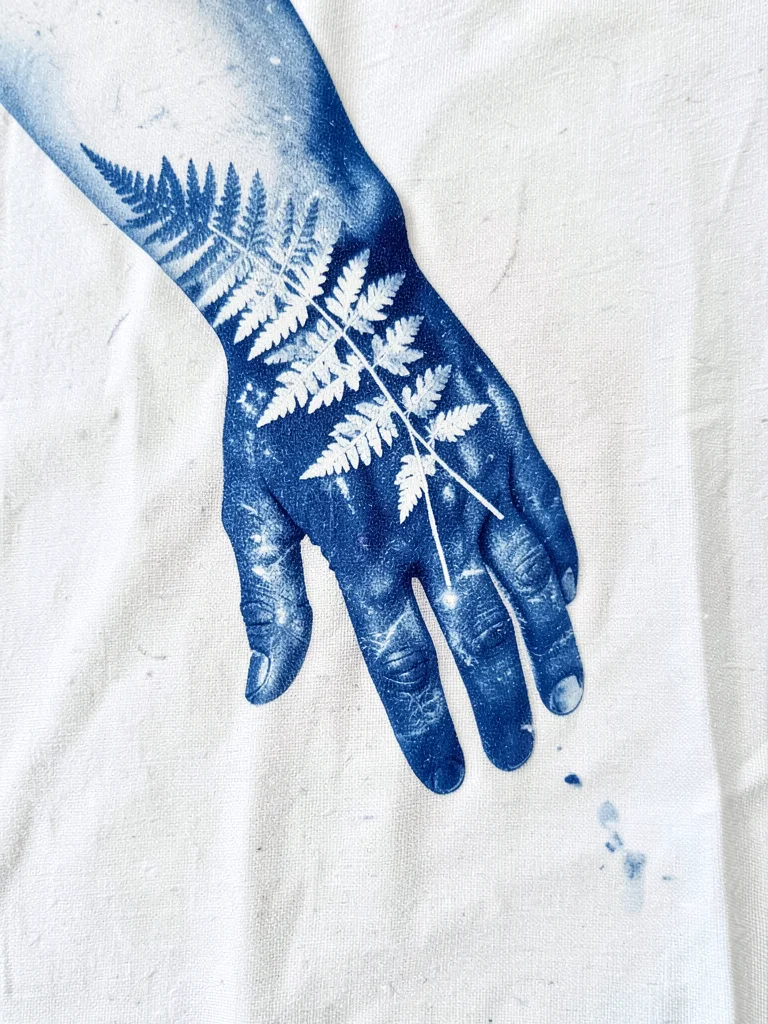A forearm and hand reaching down — body print on cotton, botanical fern overlaid