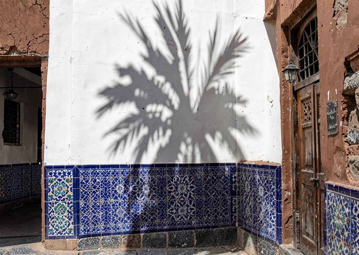 Geometric shadow play in Marrakech medina, whitewashed wall with deep blue tiles