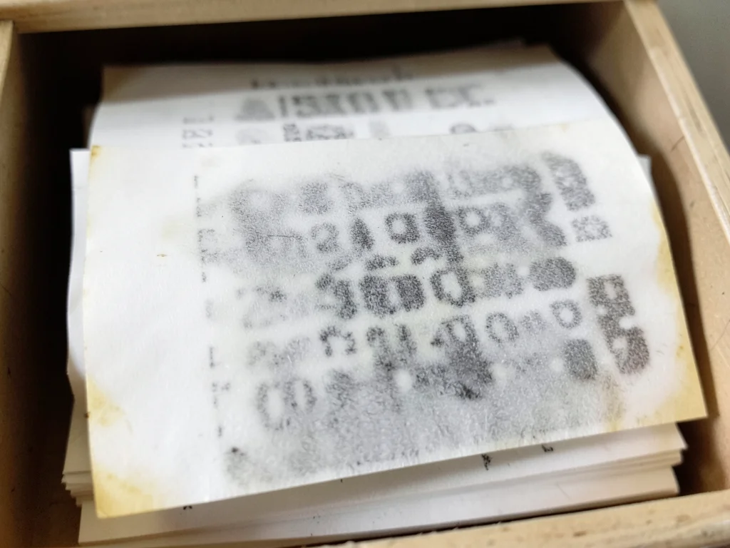 Stack of old thermal receipts in a drawer, varying stages of fade from crisp bla