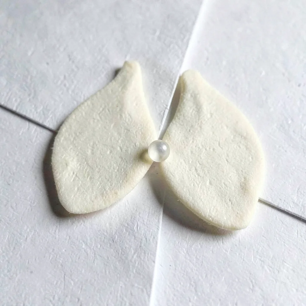 Two cream tongues meeting at a sharp diagonal seam, single bead of light running