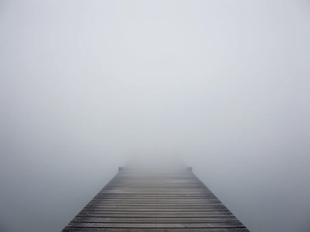Foggy pier extending into nothingness, wooden planks vanishing into grey