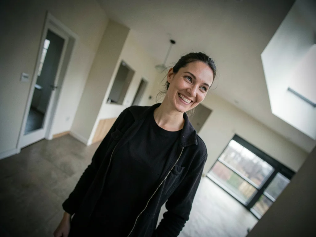 Real estate agent alone in an empty house, her smile at an angle that matches no