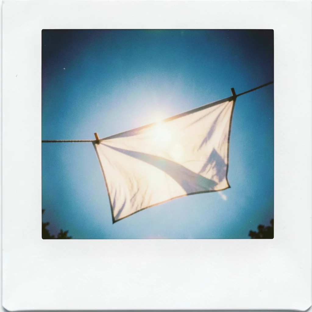 A clothesline with a single white sheet billowing in wind, blue sky behind, sun 