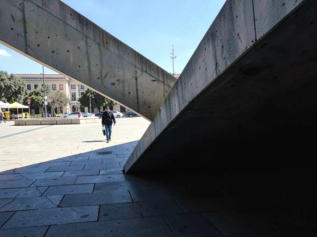 Sharp diagonal shadow of a brutalist cantilever slicing a public plaza into brig