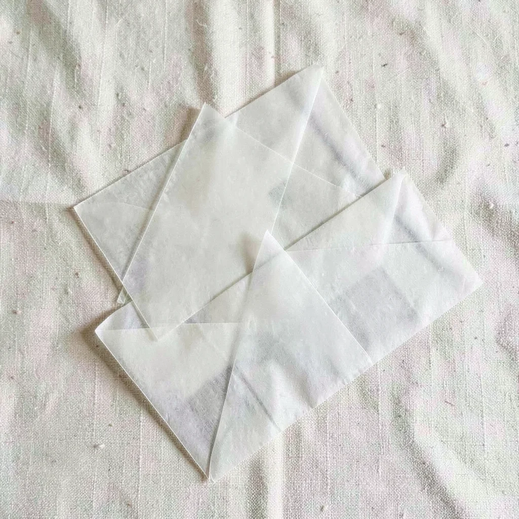 Top-down arrangement of three glassine envelopes stacked unevenly on cream linen