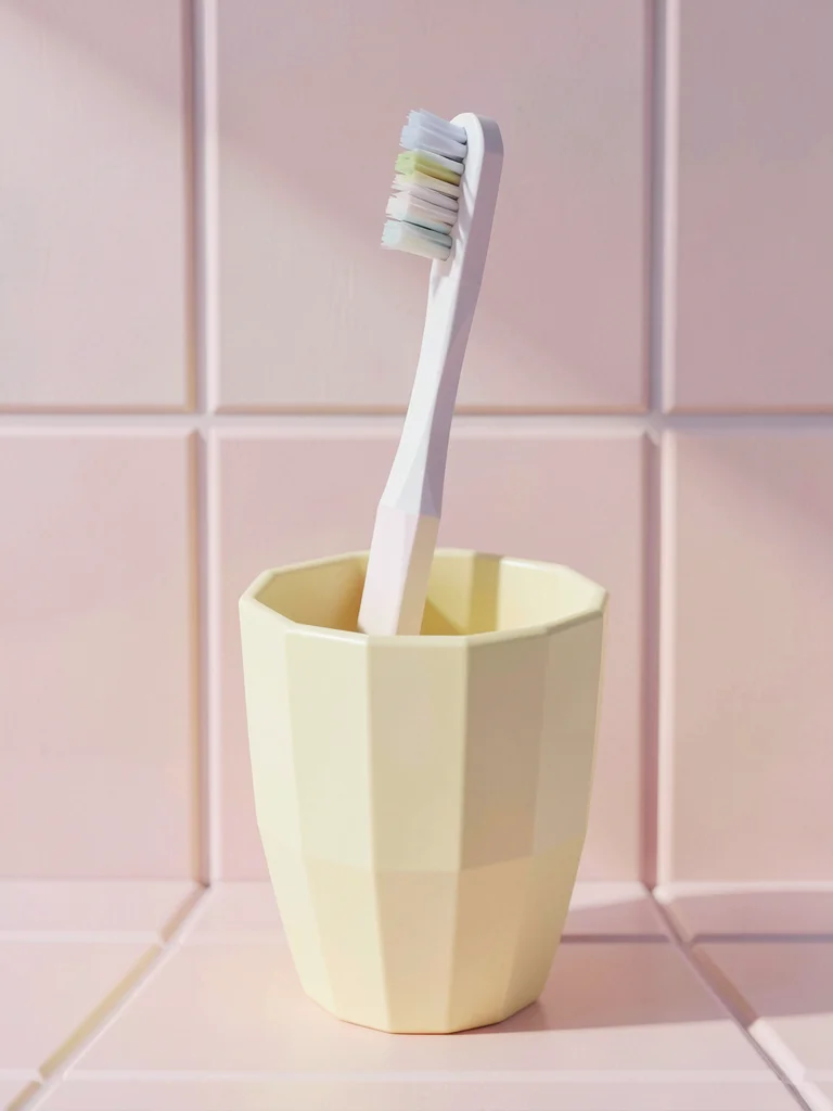 Solo faceted toothbrush standing in a butter-yellow cup against pastel pink tile