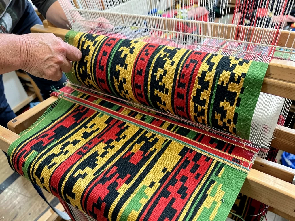 Traditional hand loom in use — shuttle mid-pass through colored warp threads