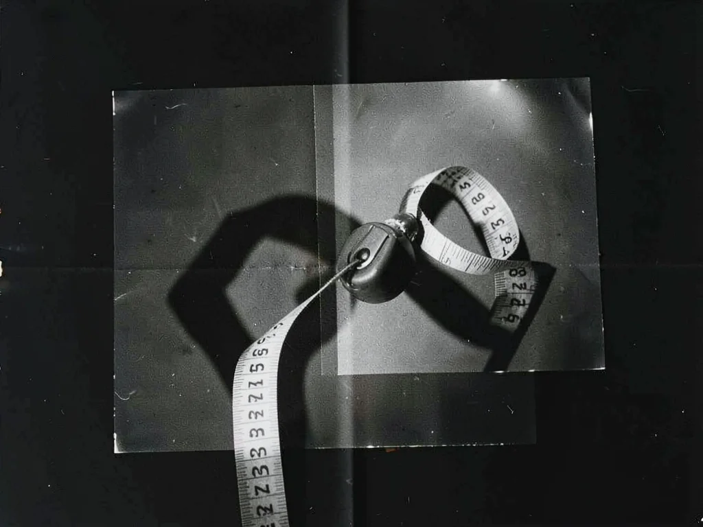 A photogram of a tape measure unspooled — numerals absent, only the shadow form