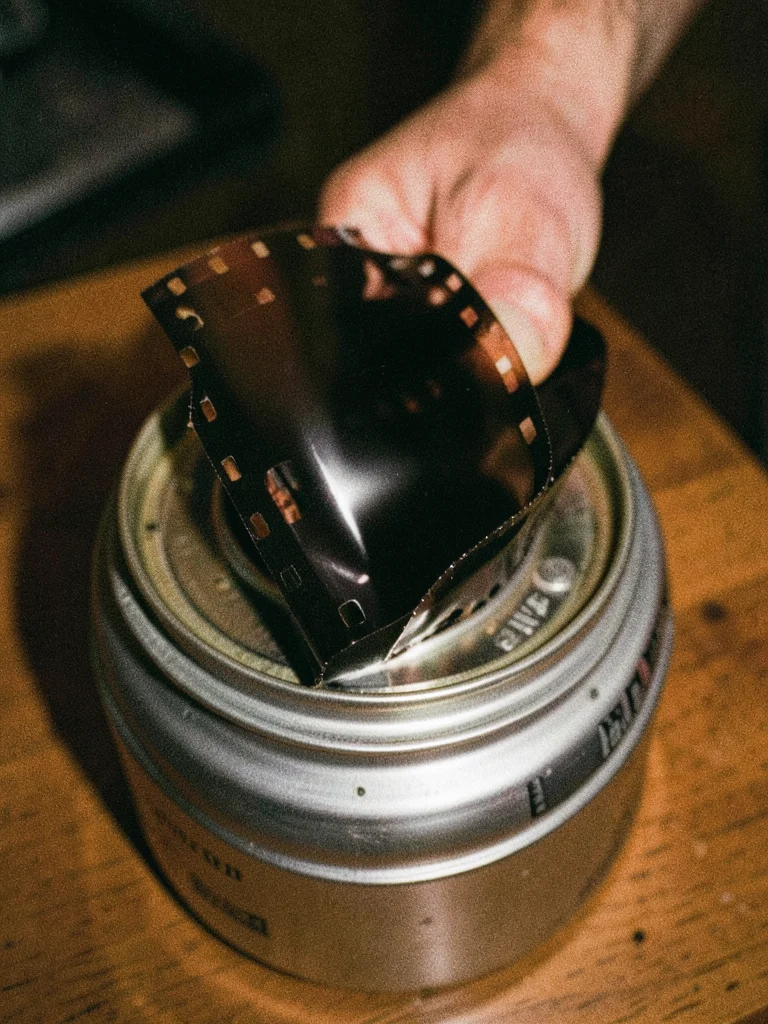 Roll of 35mm film partially pulled from canister, sprocket holes and leader tong