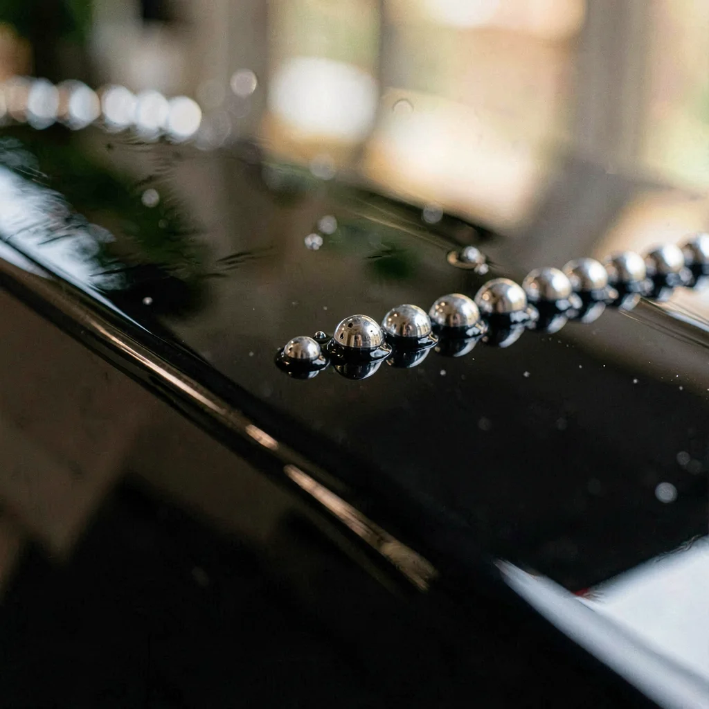 Macro of beaded water rolling across a freshly waxed black hood, soft silver hig
