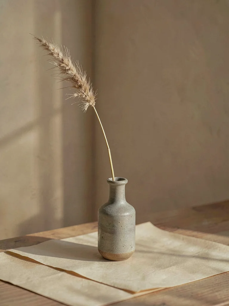 One slender dried grass stem with feathery seed-head rising from small stoneware