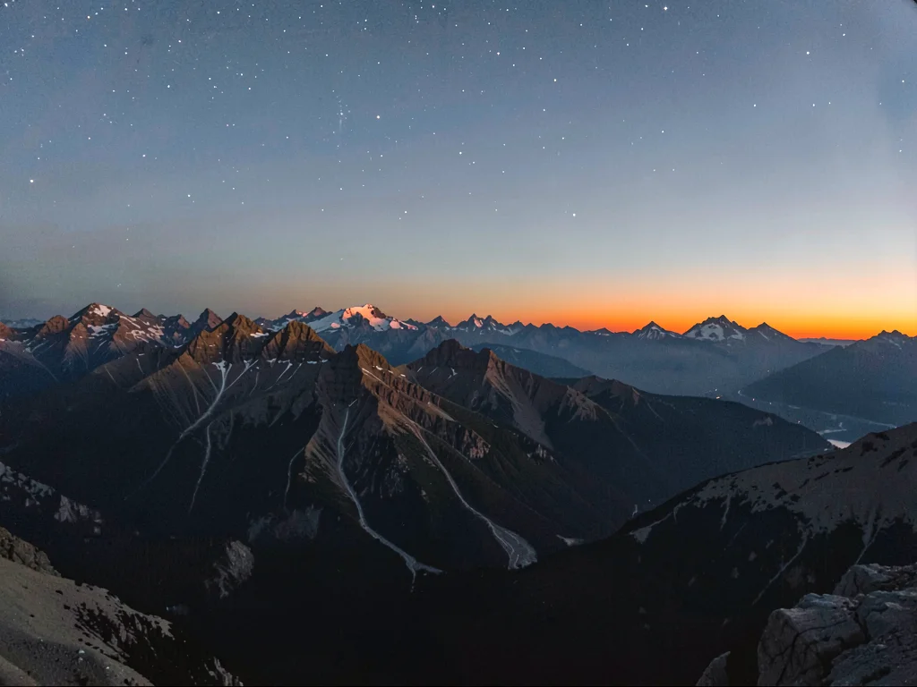 Alpenglow on distant peaks while upper sky shows faint stars