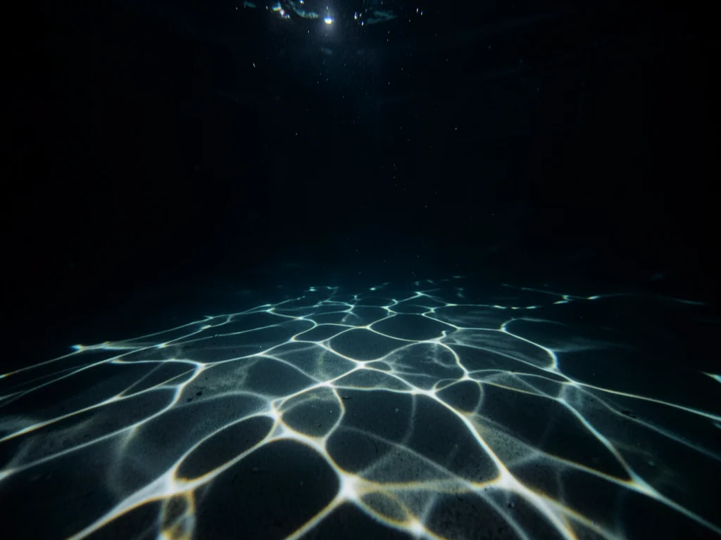 Flashlight underwater in dark pool, caustic light patterns on pool floor