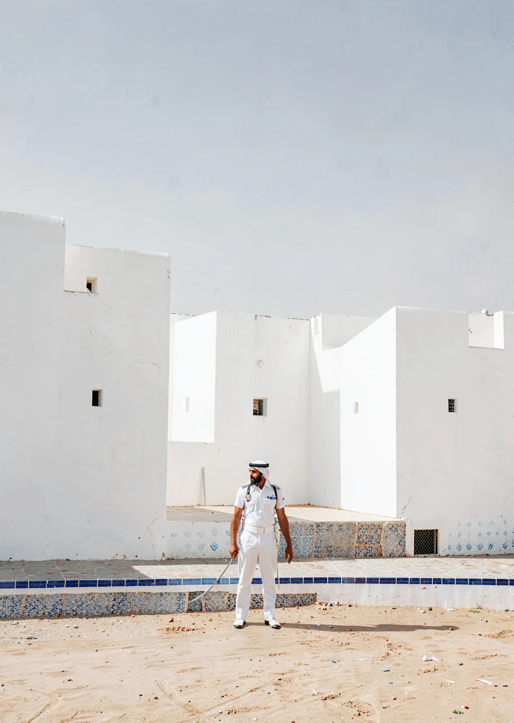 Extreme minimalist restraint of Muscat, Oman, royal guard in white, fort wall ba