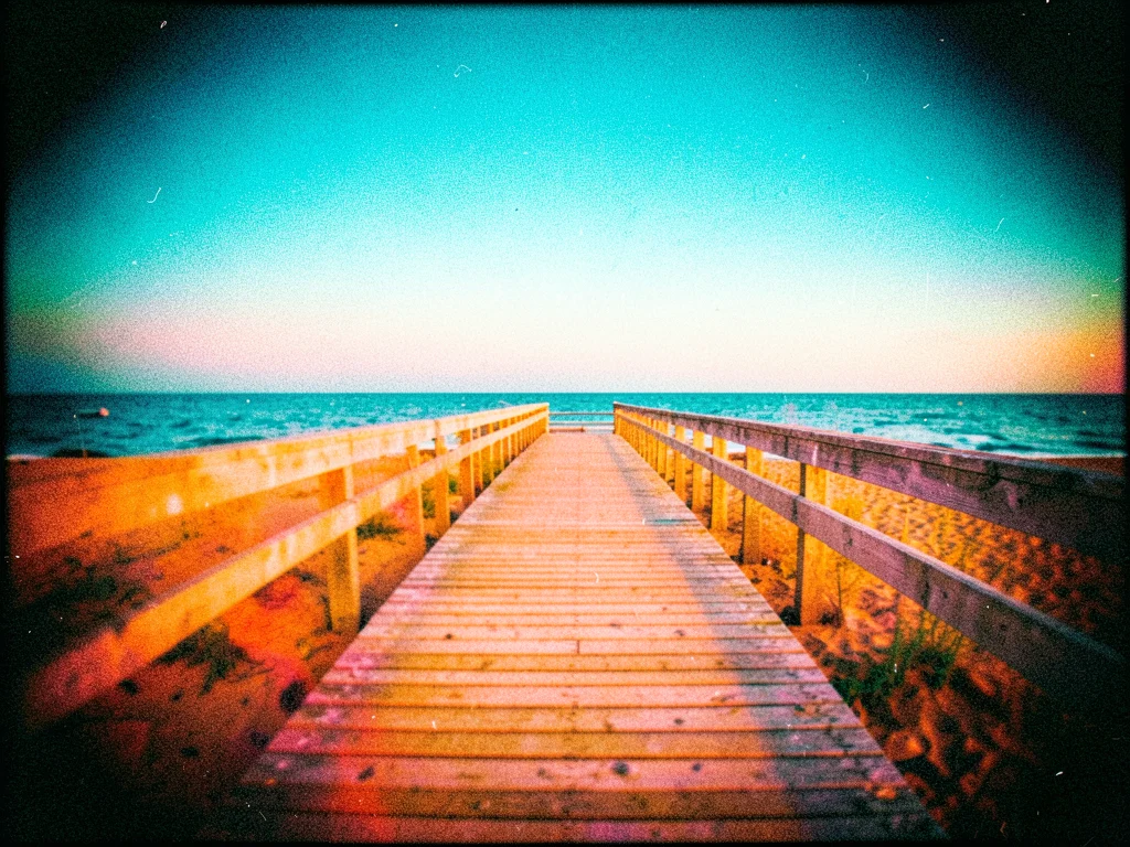 A beach boardwalk at sunset, the planks leading to the sea, colors pushed to cya