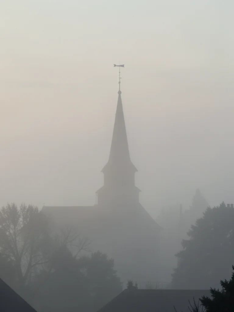 A church spire emerging from a blanket of fog, only the top 20 feet visible, a w