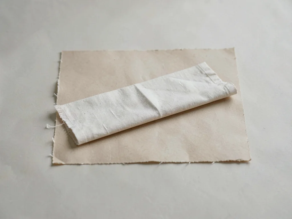 One unbleached linen napkin folded into a long rectangle on beige paper, edge fr