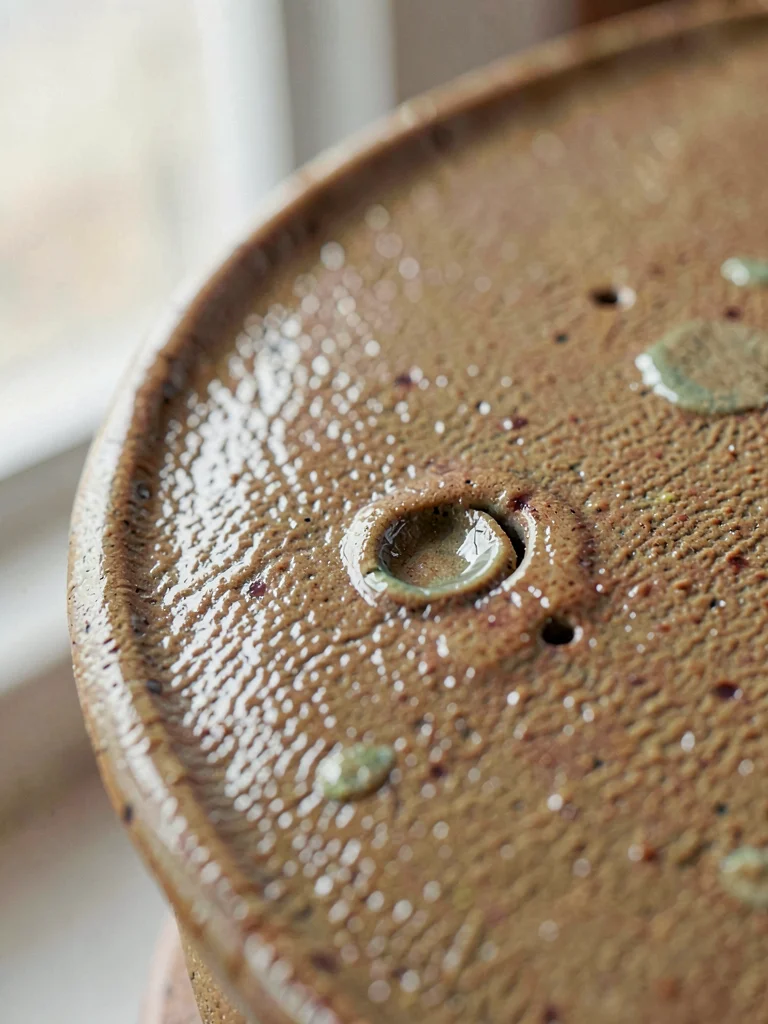 Salt-glazed stoneware curve, pebbled skin punctuated by a deep hand-pressed dent
