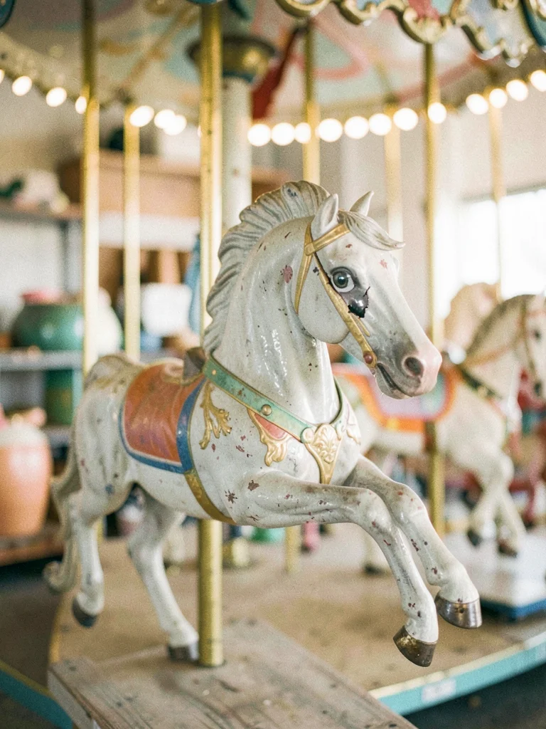 Paint-chipped carousel horse in storage, one glass eye cracked, gilt faded to gr