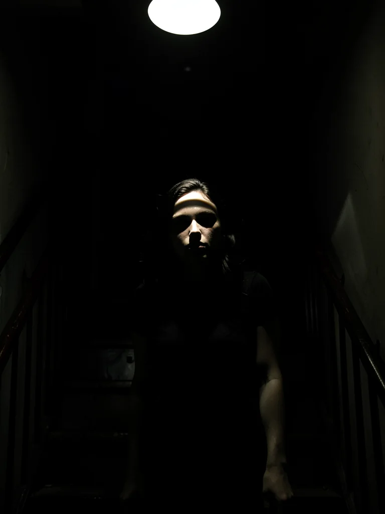 Woman descending staircase, single overhead light creating stripe across her eye