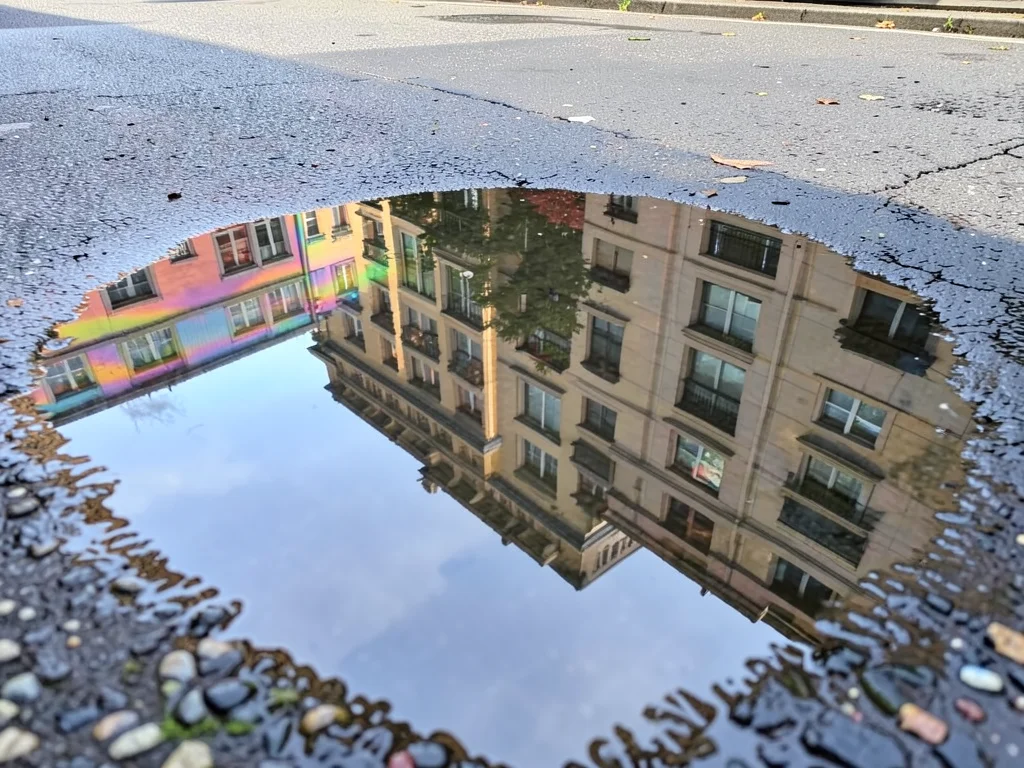 Building facade reflected in puddle with oil film, architecture visible through 