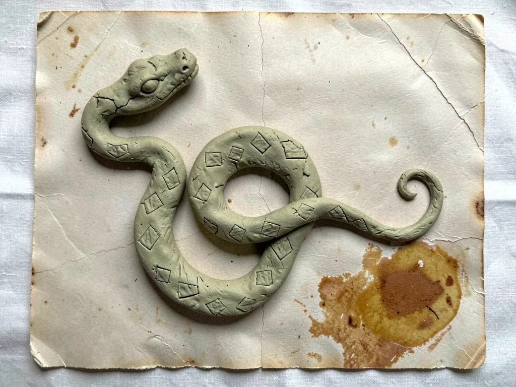 Coiled pressed-clay snake with diamond markings, head at the upper left corner, 