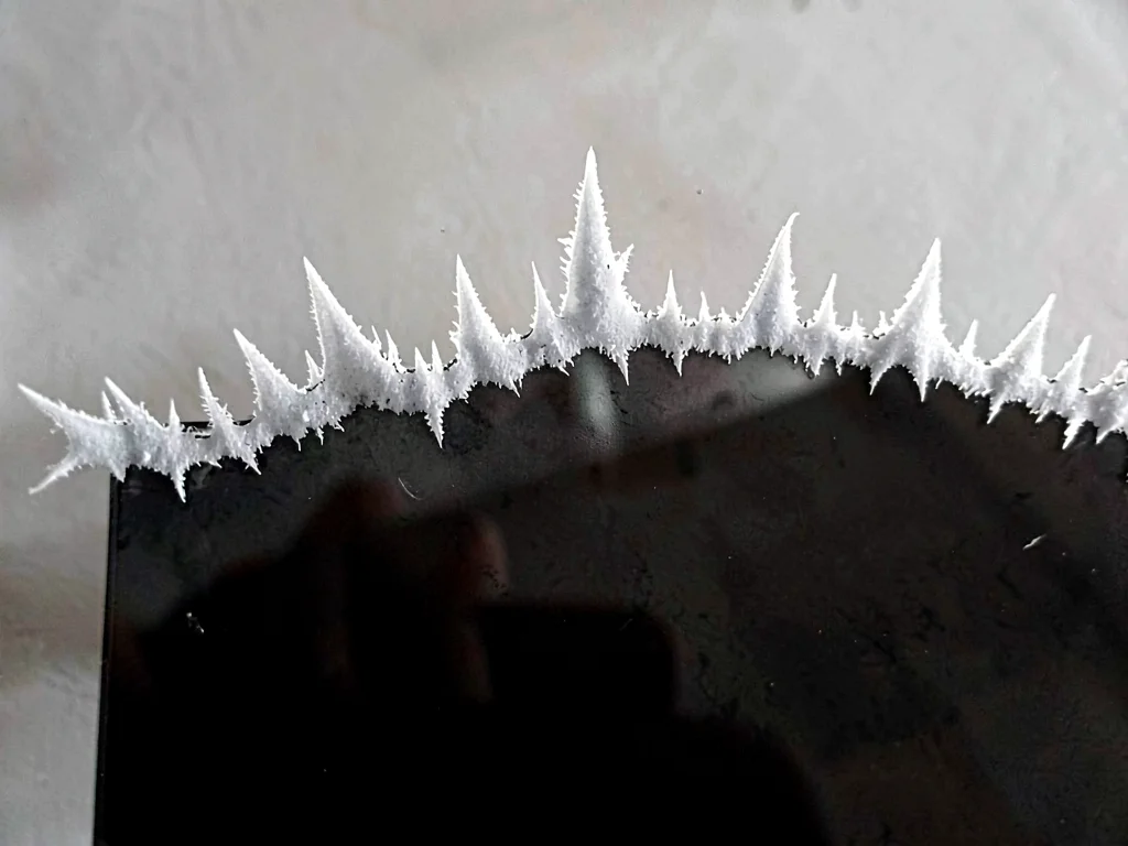 Hoar-fringe ridge running across the upper edge of a cold black glass plate, eve