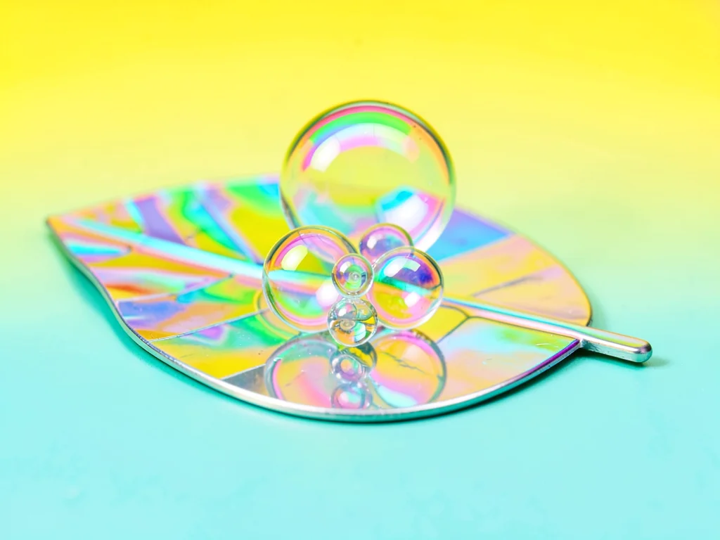 Tiny bubble cluster perched on a leaf-shaped chrome disc against a banana-yellow