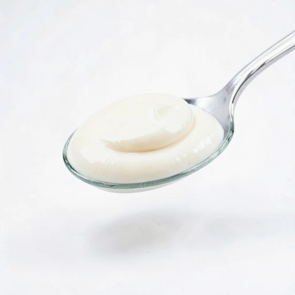 Clean studio macro of a smooth cream texture being lifted on a glass spatula, so