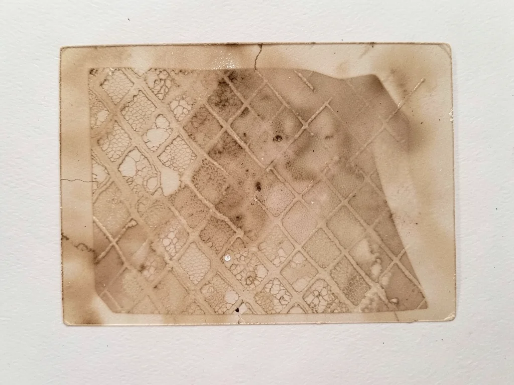 Ghost pull of a monoprint featuring pressed lace texture, faint diamond pattern 