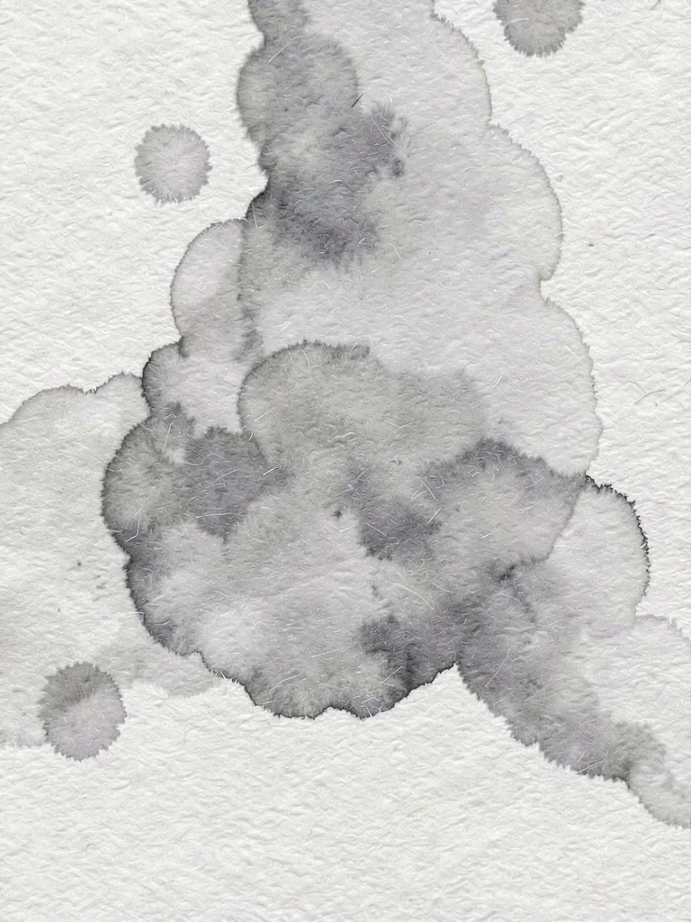 Abstract ink bloom dispersing across cold-press cotton as soft grey cloud diffus