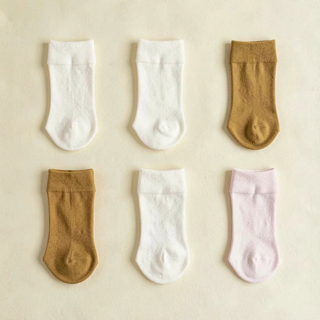 Color-block grid flatlay of six folded socks tubes in alternating cream and must