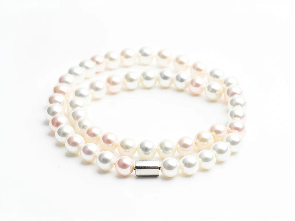 Pearl necklace coiled on white surface, each pearl catching light differently, c