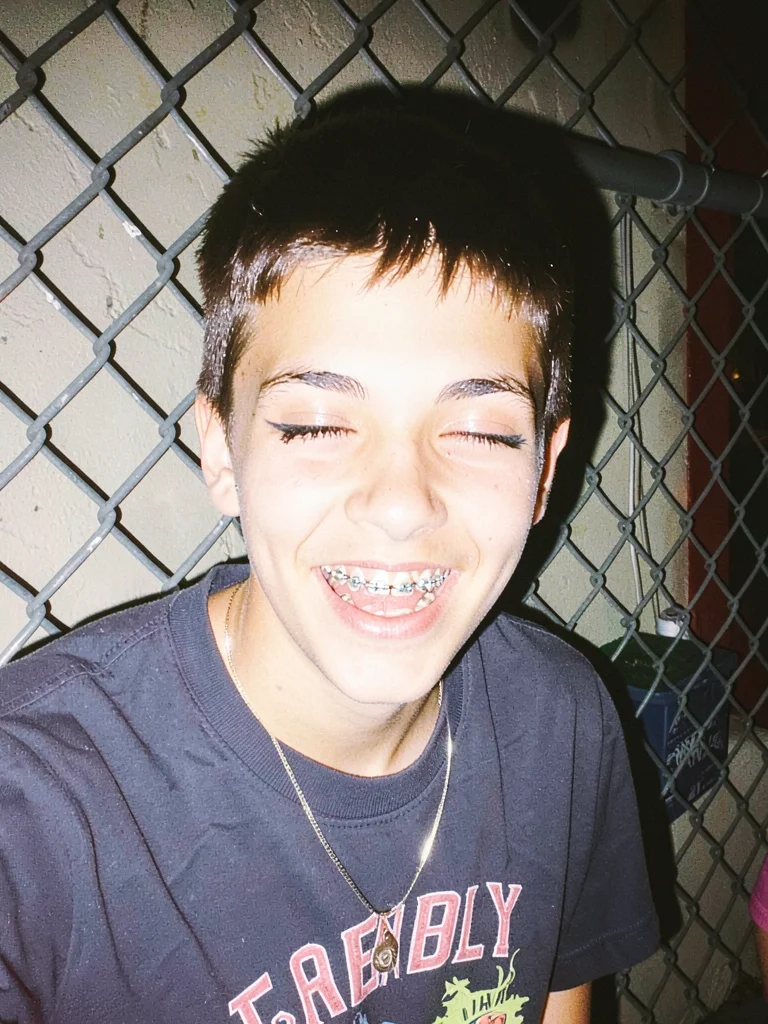 Teenager with smeared mascara laughing against a chain-link fence, flash reflect