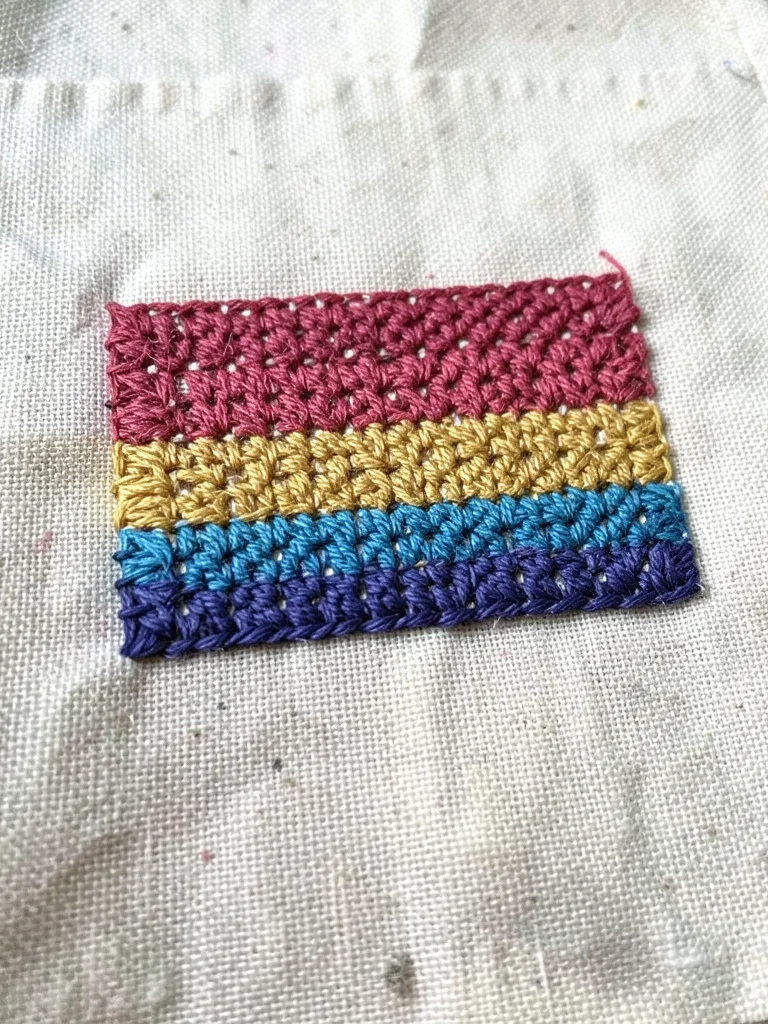 Hand-stitched pride flag on cotton, each stripe a different thread texture