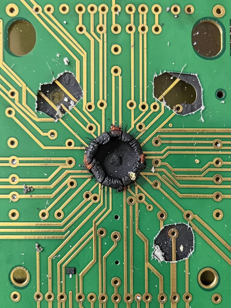 A damaged PCB with a burnt component leaving a dark scorch mark on the green sol