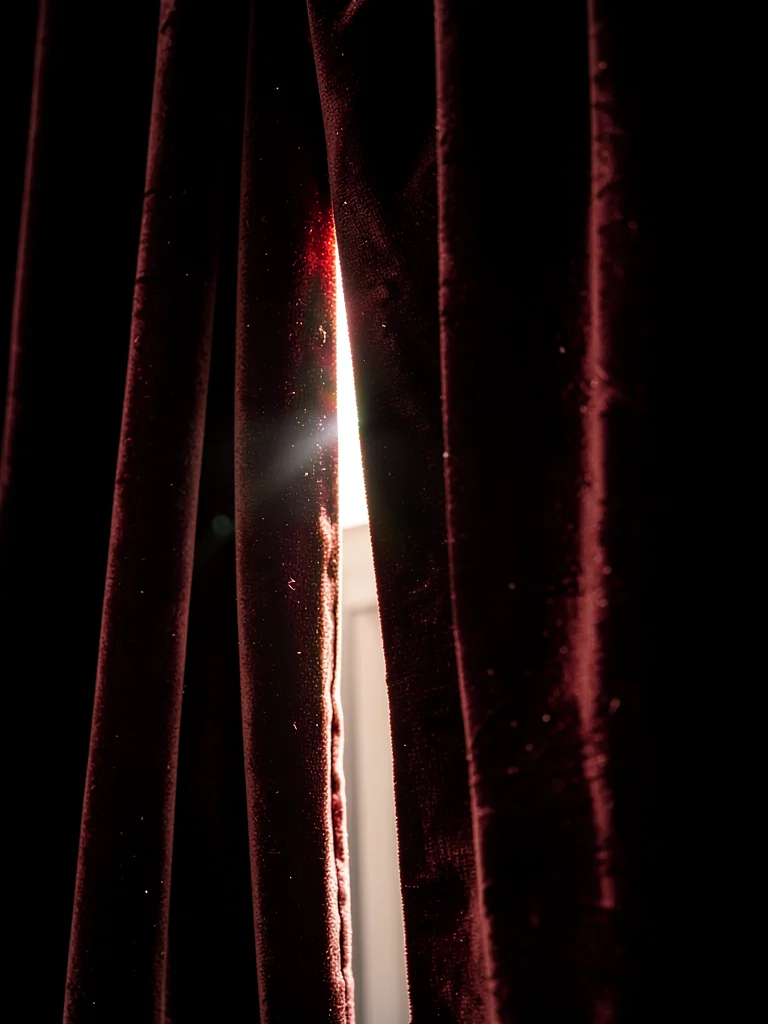 Velvet curtain partially drawn, light streaming through gap, theatrical reveal