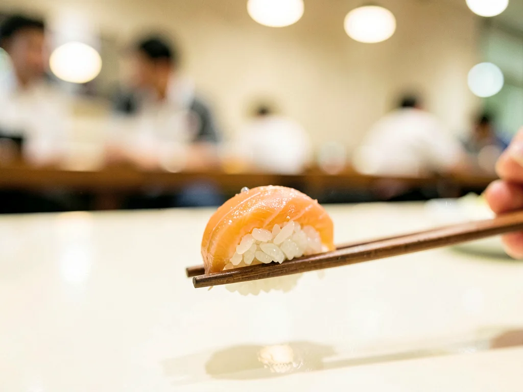 Sushi piece on chopsticks, restaurant behind cream