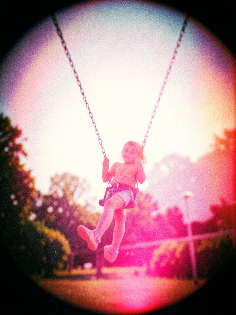 A child on a swing at the peak of its arc, the chain blurred, the figure sharp f