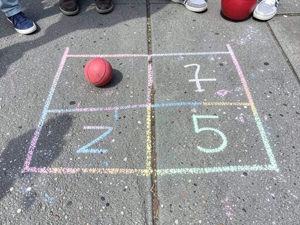 A game of four-square drawn in chalk, the squares numbered, a bouncy ball in one