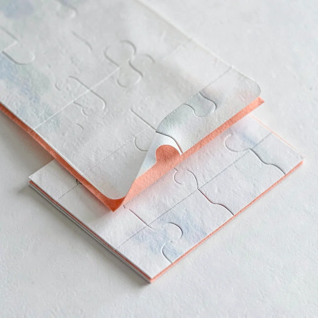 Stacked trio of translucent puzzle pages offset diagonally, top sheet curling to