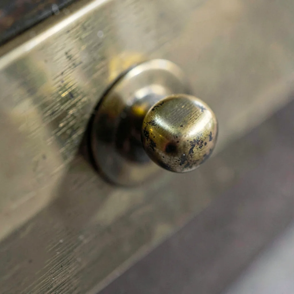 Macro of an unlacquered brass cabinet pull with hand-rubbed patina along the thu