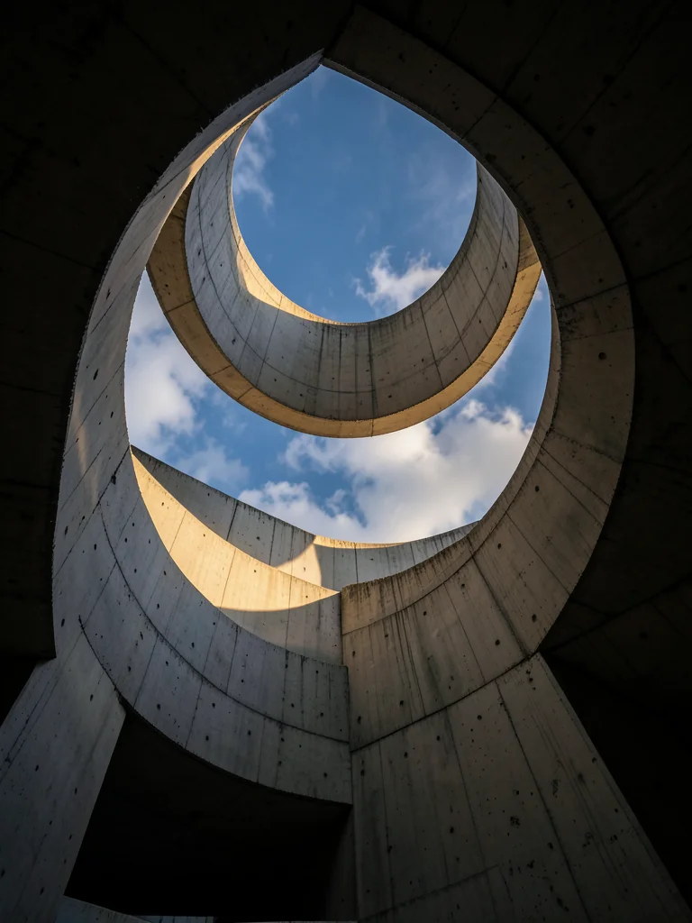 A concrete spiral staircase viewed from below, the helix ascending toward a circ