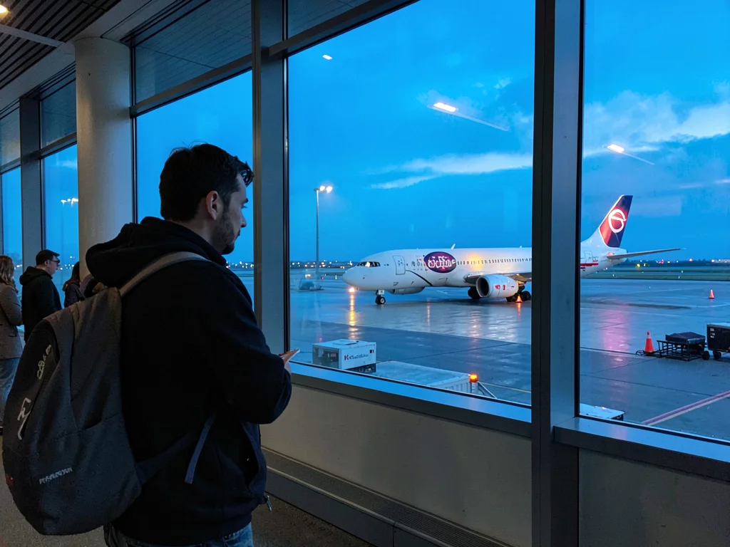 Traveler at terminal window watching plane taxi at blue hour