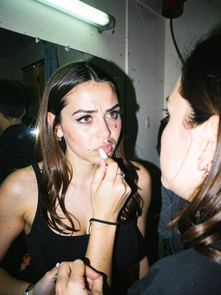 Woman reapplying lipstick in a dive bar bathroom, harsh fluorescent mixing with 