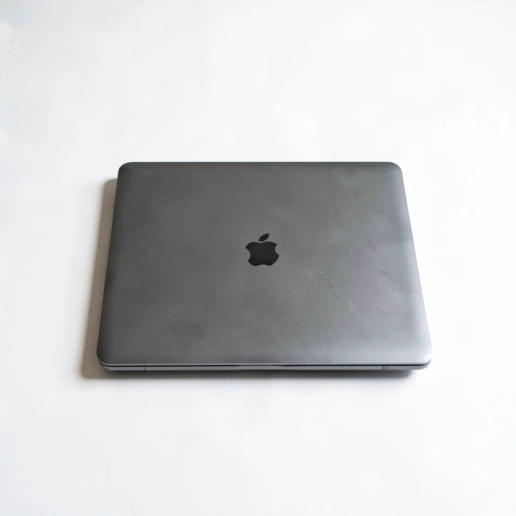 White-on-white still of a single closed laptop centered on a chalk desk, hairlin